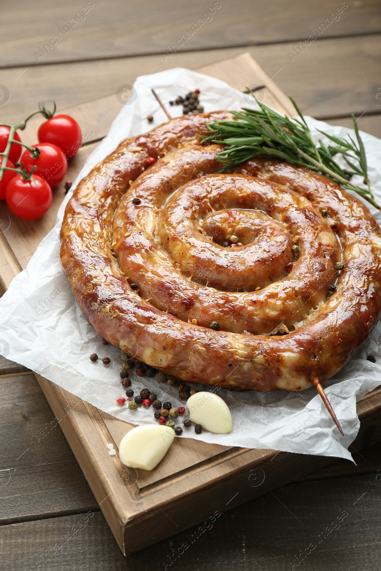 Photo of Delicious homemade sausages with spices and tomatoes on wooden table