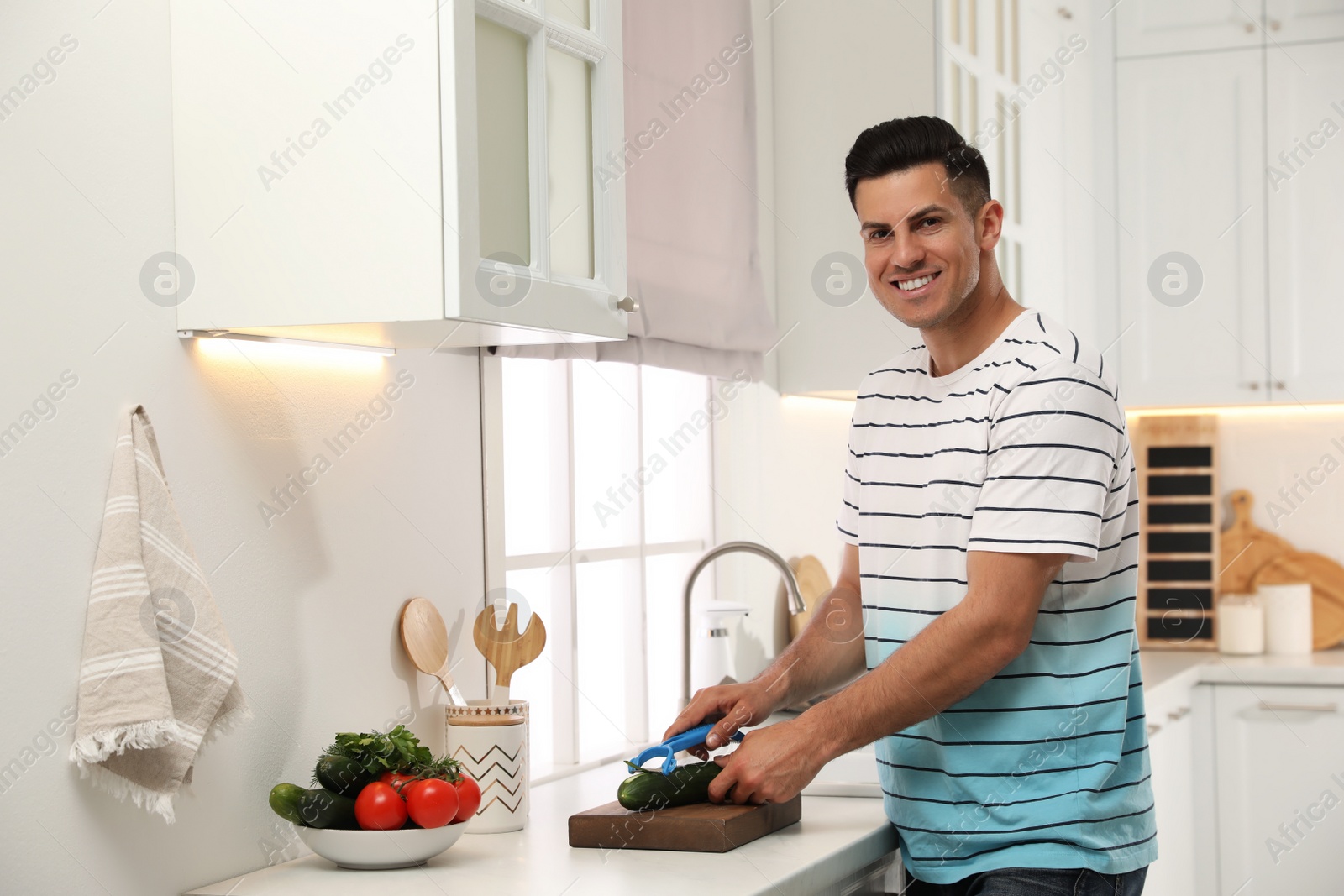 Photo of Man peeling cucumber at kitchen counter. Preparing vegetable