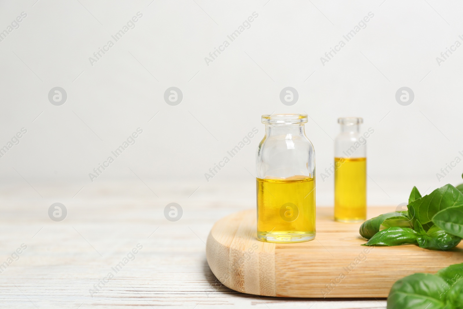 Photo of Wooden board with glass bottles of basil oil, leaves and space for text