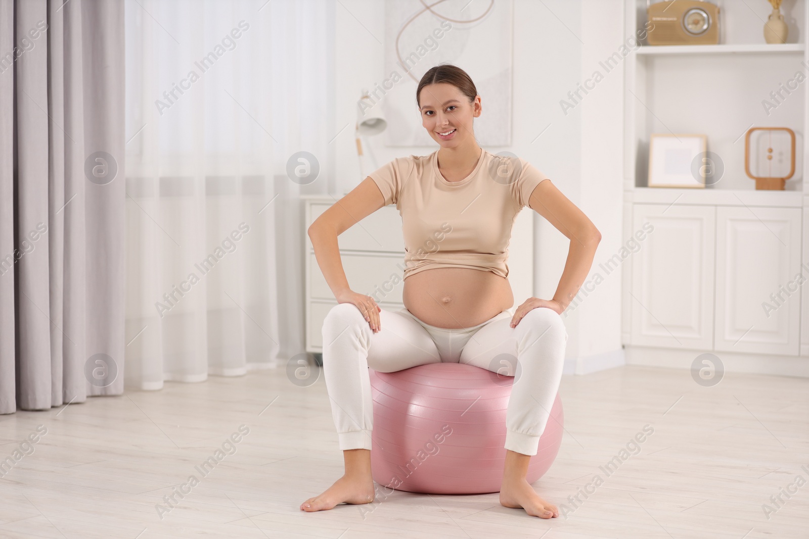 Photo of Pregnant woman sitting on fitness ball in room. Home yoga