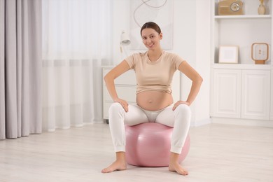 Pregnant woman sitting on fitness ball in room. Home yoga