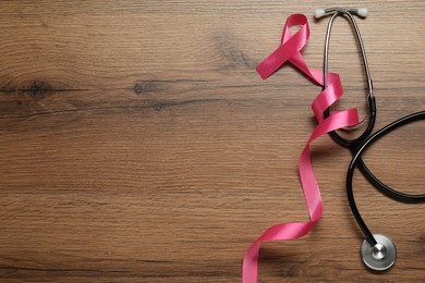 Photo of Breast cancer awareness. Pink ribbon and stethoscope on wooden table, flat lay. Space for text