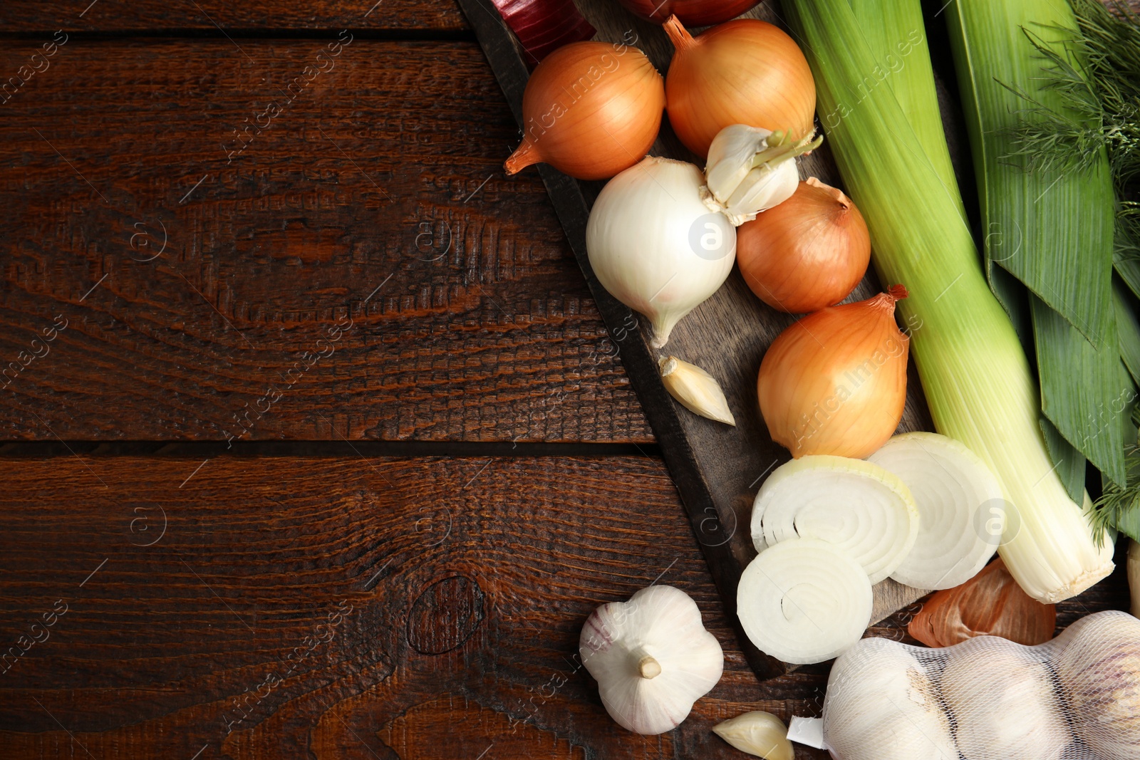 Photo of Fresh onion bulbs, leeks, garlic on wooden table, flat lay. Space for text