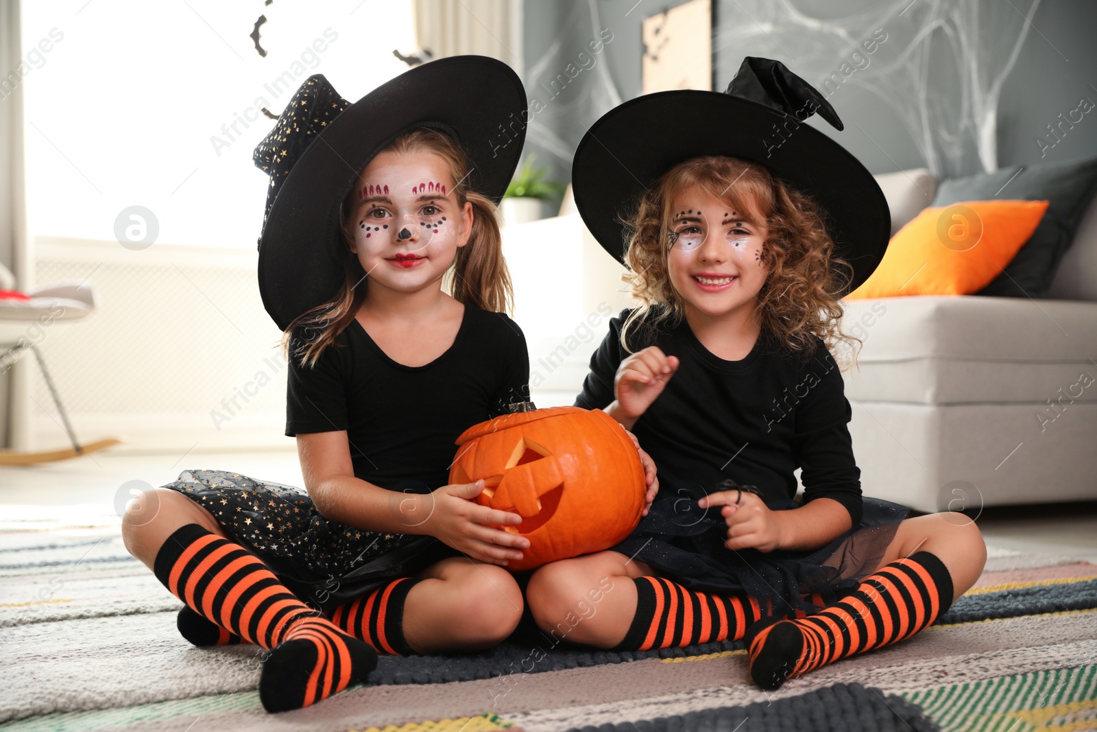 Photo of Cute little girls with pumpkin head jack lantern wearing Halloween costumes at home