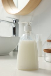 Dispenser of liquid soap on white table in bathroom