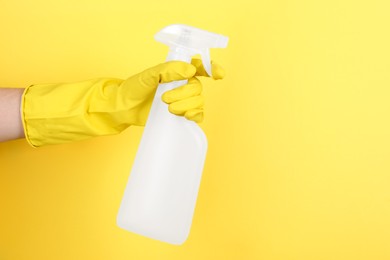 Photo of Woman holding plastic spray bottle on yellow background, closeup. Space for text