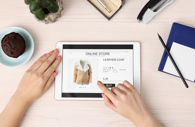 Woman with tablet shopping online at white wooden table, top view