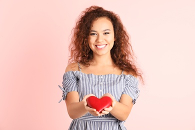 African-American woman holding wooden heart on color background