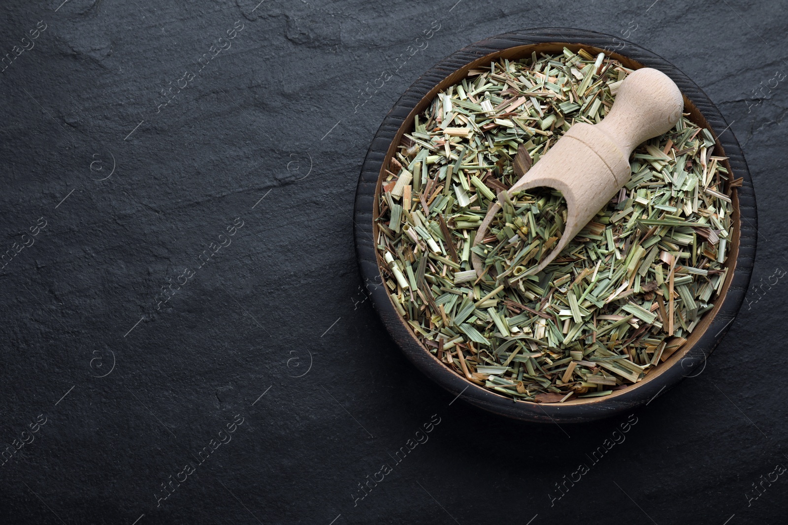 Photo of Bowl with aromatic dried lemongrass and scoop on black table, top view. Space for text