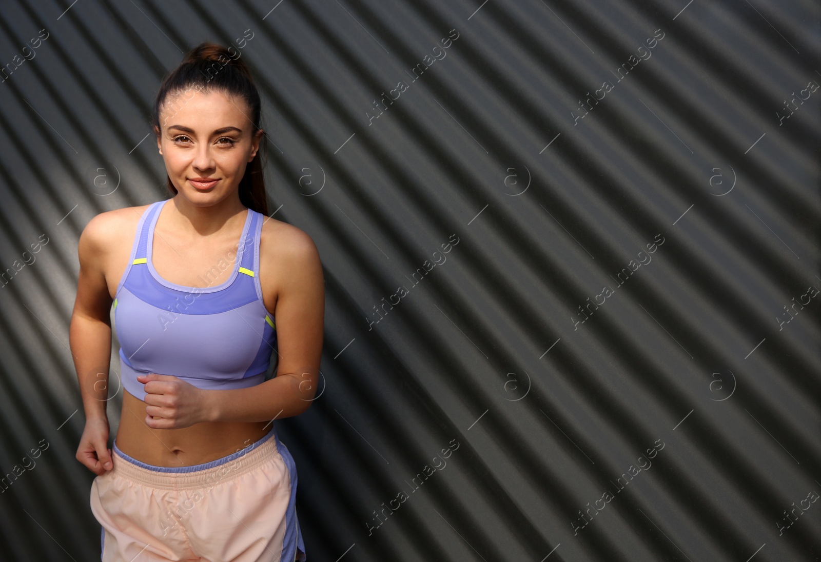 Photo of Young woman in sportswear running near corrugated metal wall. Space for text