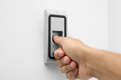 Young man pressing fingerprint scanner on alarm system indoors