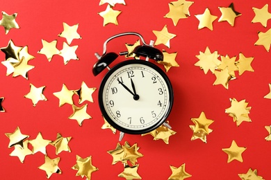 Alarm clock and golden confetti on red background, flat lay. New Year countdown