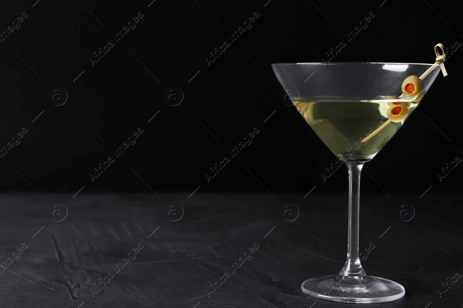 Photo of Glass of Classic Dry Martini with olives on dark table against black background. Space for text