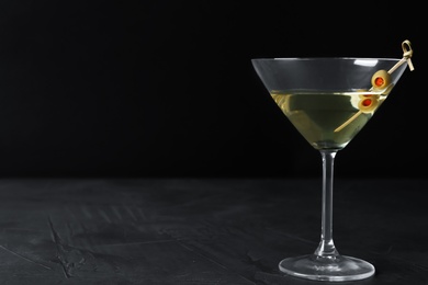 Photo of Glass of Classic Dry Martini with olives on dark table against black background. Space for text