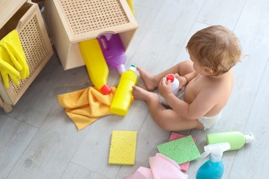 Photo of Cute baby playing with bottle of detergent on floor at home, above view. Dangerous situation