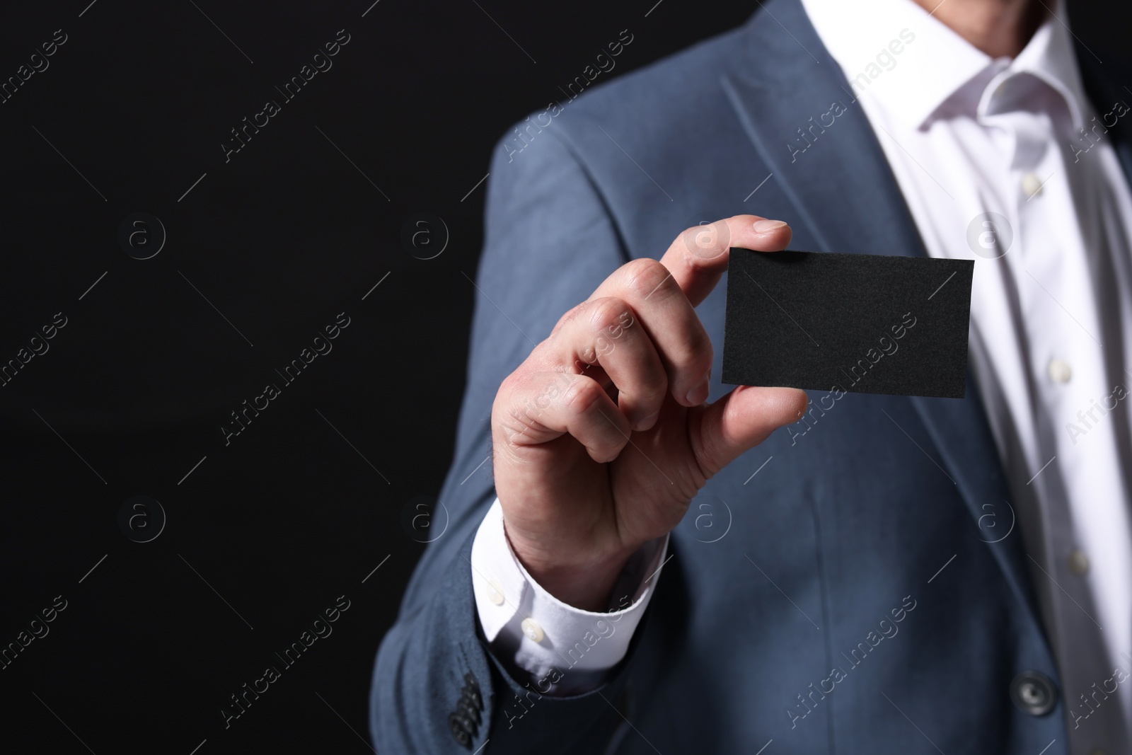 Photo of Businessman holding blank business card on black background, closeup. Space for text