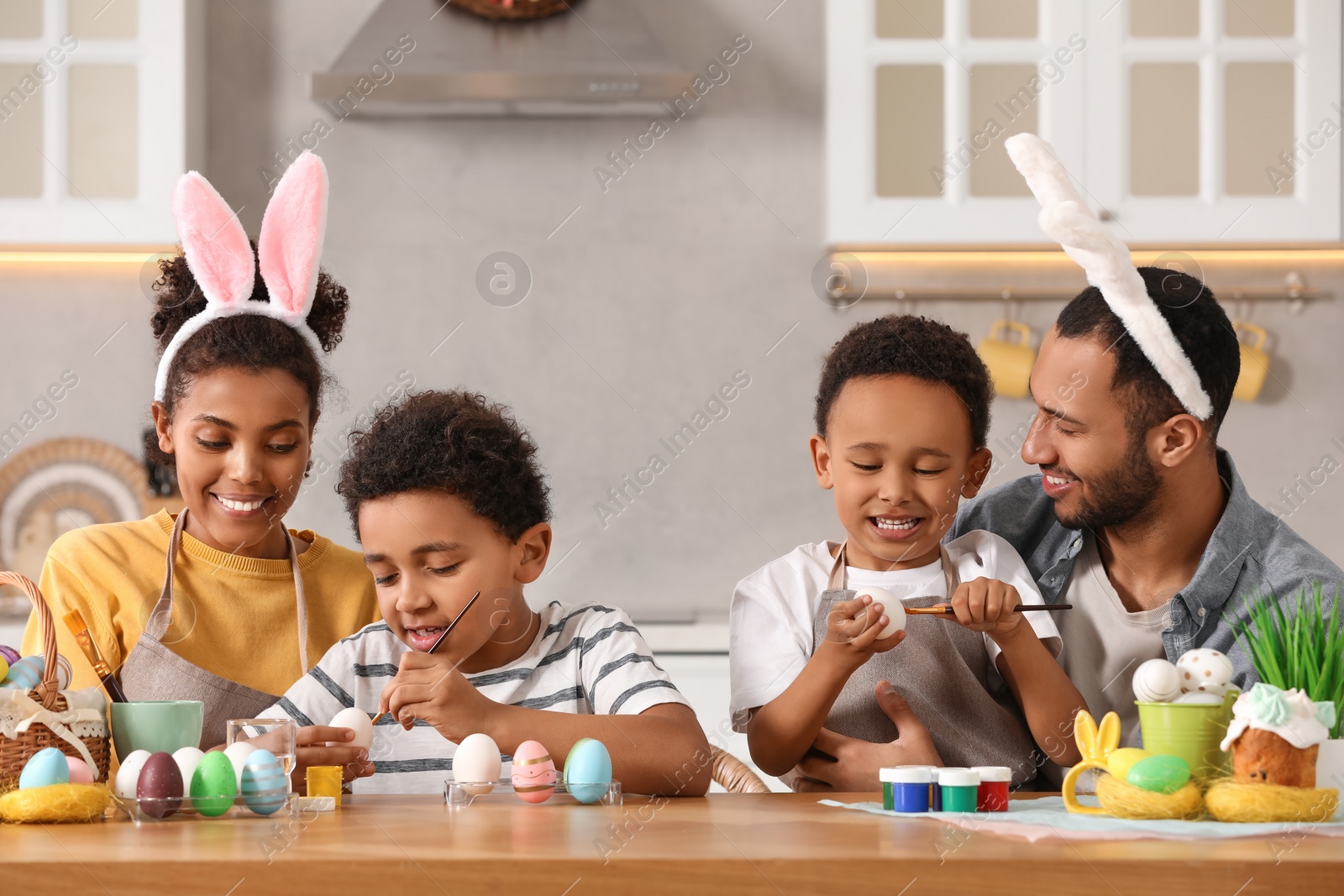 Photo of Happy African American family painting Easter eggs at table in kitchen