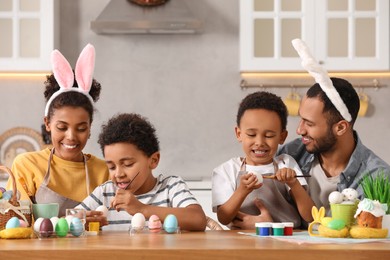 Happy African American family painting Easter eggs at table in kitchen