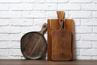 Photo of Different cutting boards on wooden table near white brick wall