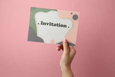 Photo of Woman holding beautiful card with word Invitation on pink background, closeup