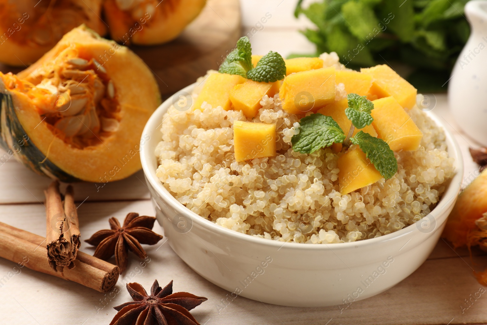 Photo of Tasty quinoa porridge with pumpkin, mint in bowl and spices on light wooden table, closeup