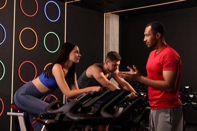 Photo of Trainer working with people in fitness club. Indoor cycling class