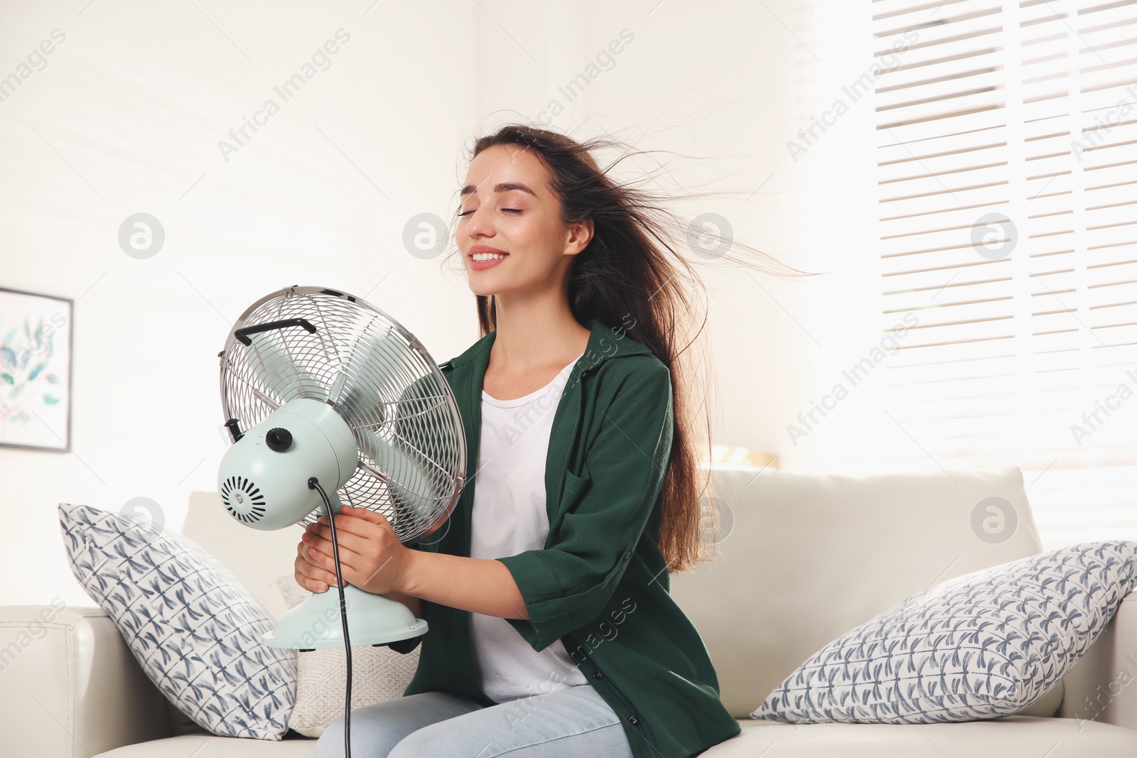 Photo of Woman with fan enjoying air flow at home. Summer heat