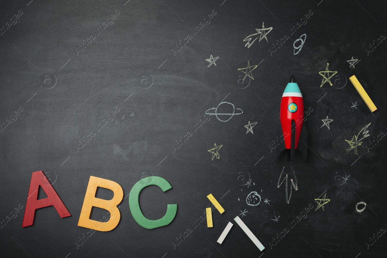 Photo of Bright toy rocket, school supplies and drawings on chalkboard, flat lay. Space for text