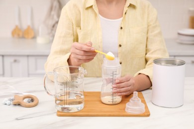 Photo of Woman preparing infant formula at table indoors, closeup. Baby milk