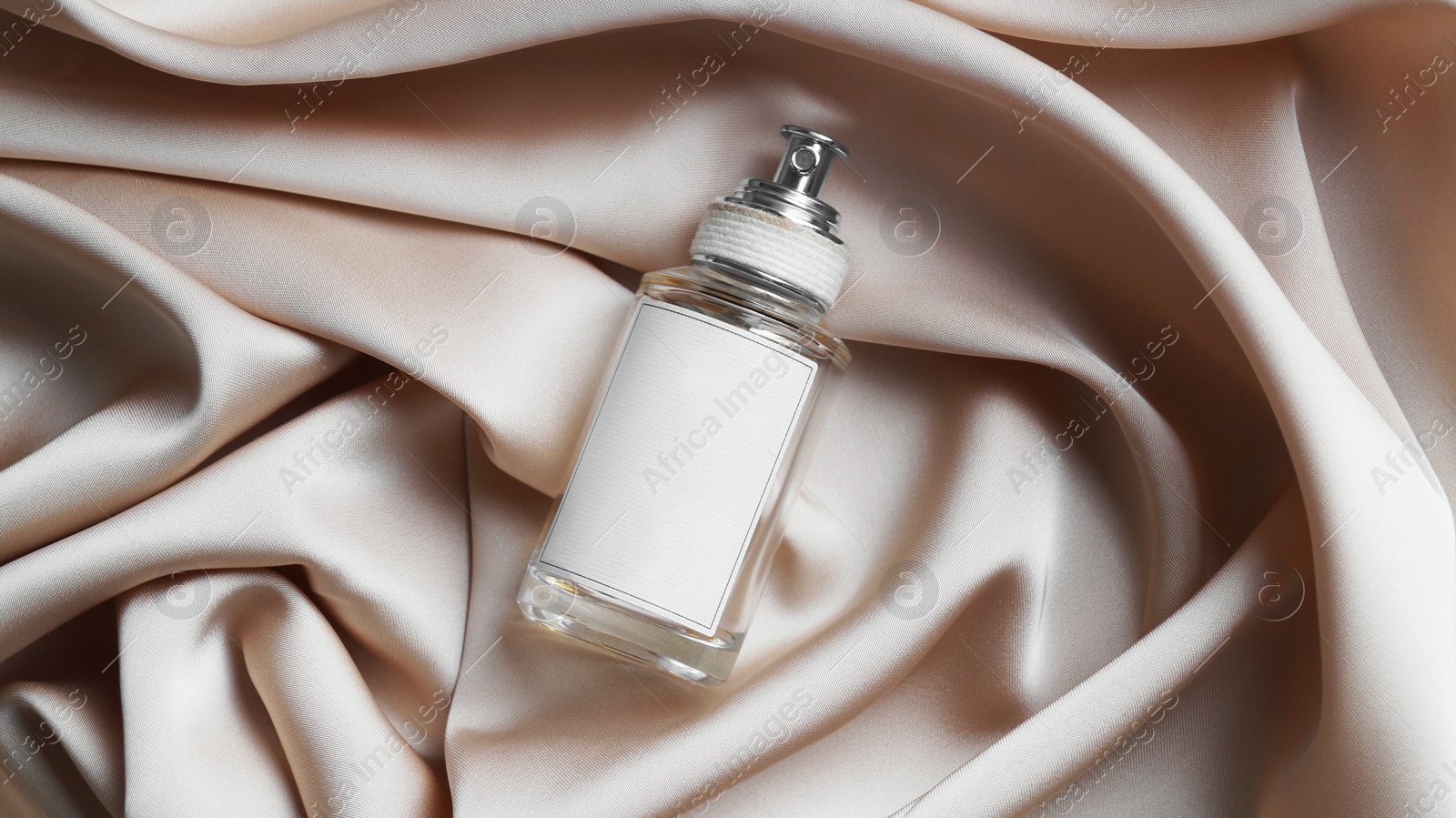 Photo of Luxury bottle of perfume on beige silk, top view