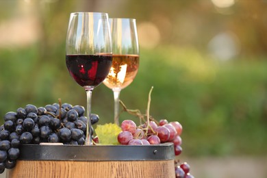 Delicious wines and ripe grapes on wooden barrel outdoors, space for text