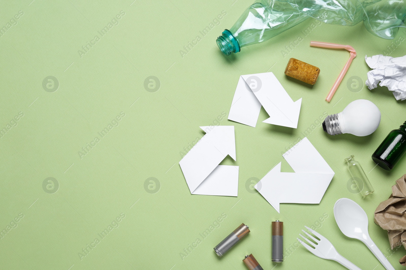 Photo of Recycling symbol and garbage on light green background, flat lay. Space for text