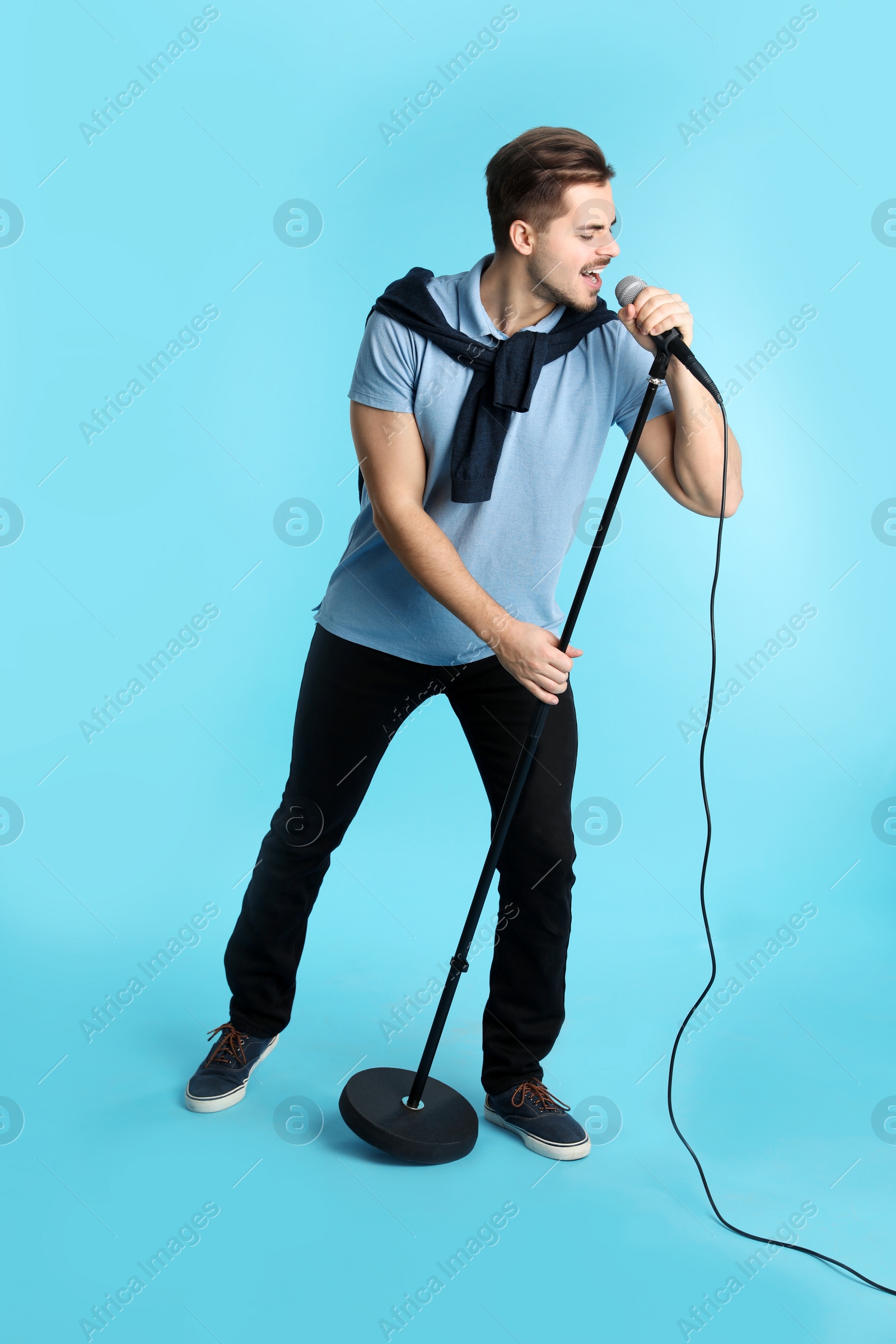 Photo of Young handsome man in casual clothes singing with microphone on color background