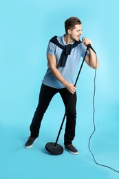 Young handsome man in casual clothes singing with microphone on color background