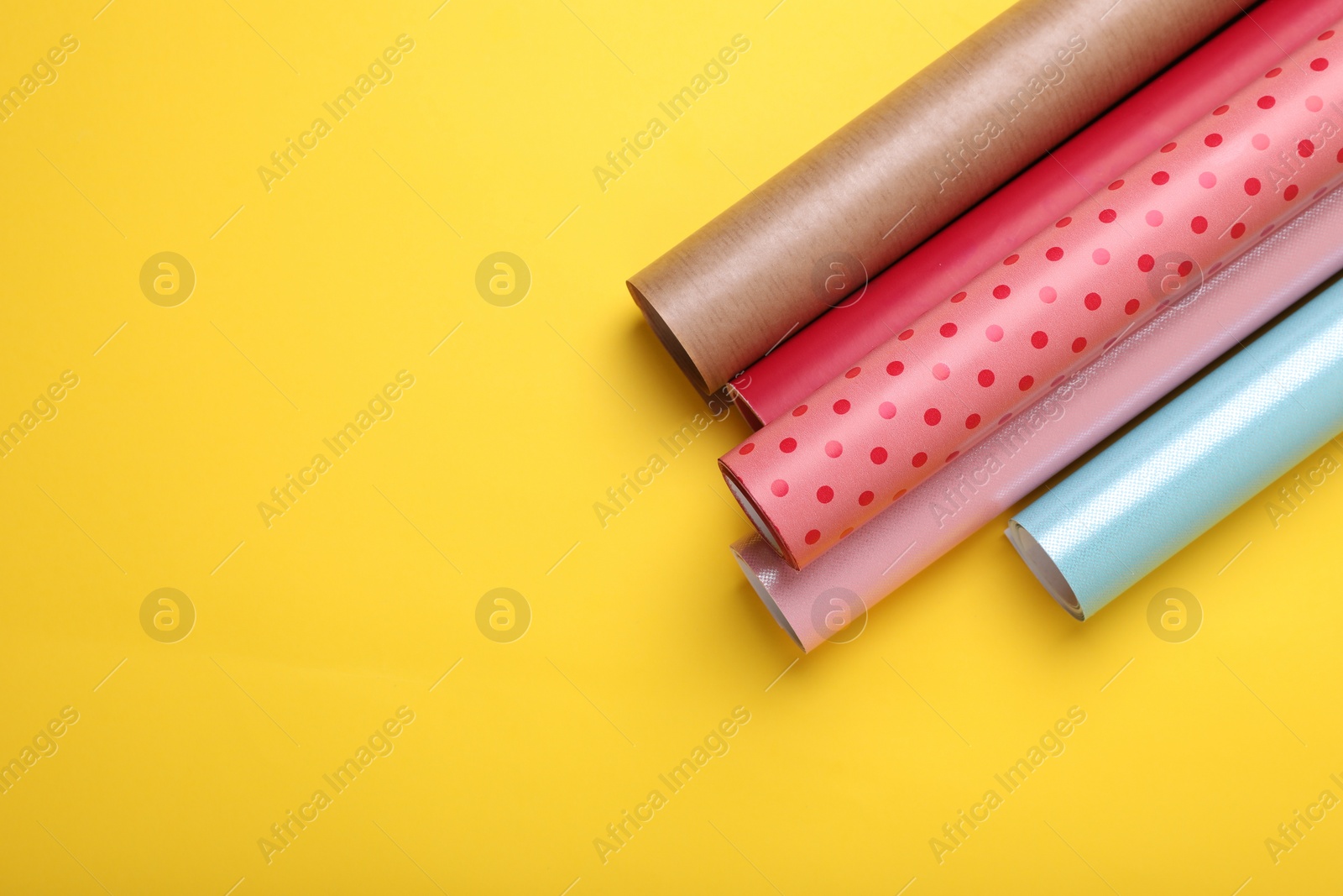 Photo of Rolls of colorful wrapping papers on yellow background, top view. Space for text