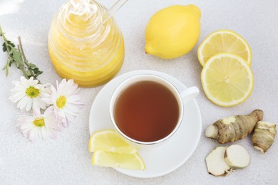 Photo of Cup of delicious tea with honey, lemon and ginger on white table, above view