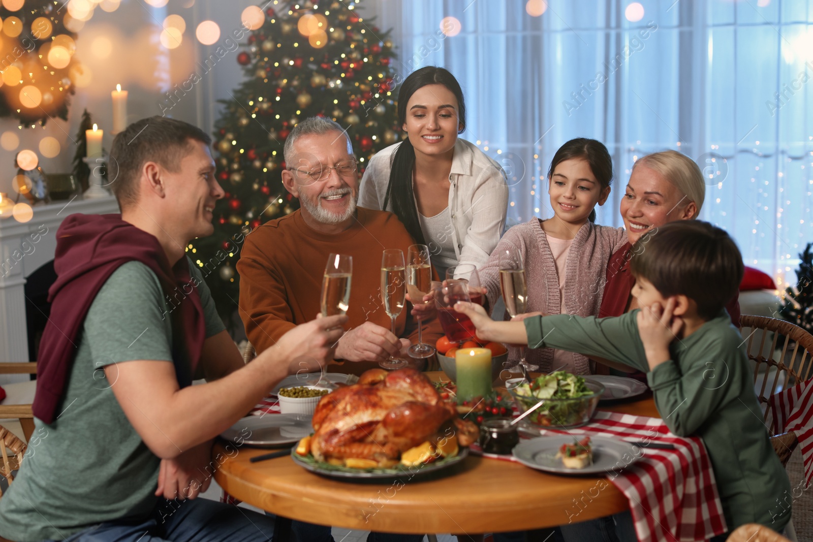 Photo of Happy family clinking glasses of drinks at festive dinner indoors, bokeh effect. Christmas celebration