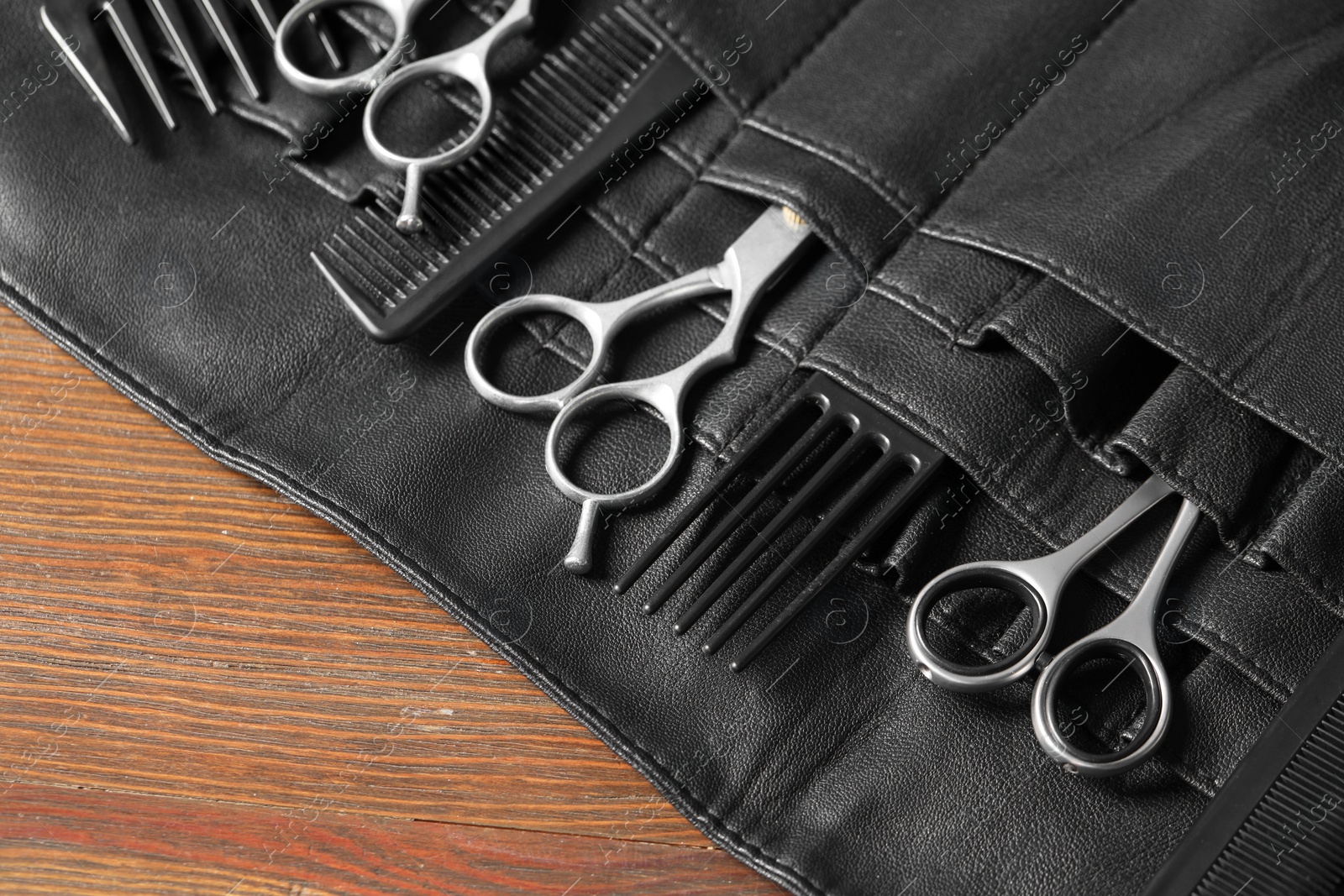 Photo of Hairdresser tools. Professional scissors and combs in leather organizer on wooden table, closeup