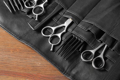 Hairdresser tools. Professional scissors and combs in leather organizer on wooden table, closeup