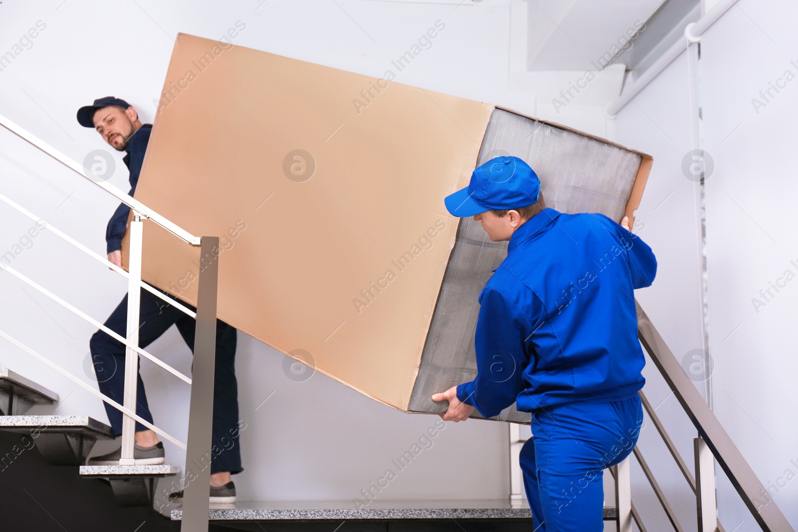 Photo of Professional workers carrying refrigerator on stairs indoors