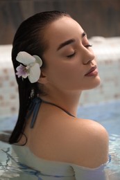 Beautiful woman with orchid flower in spa swimming pool