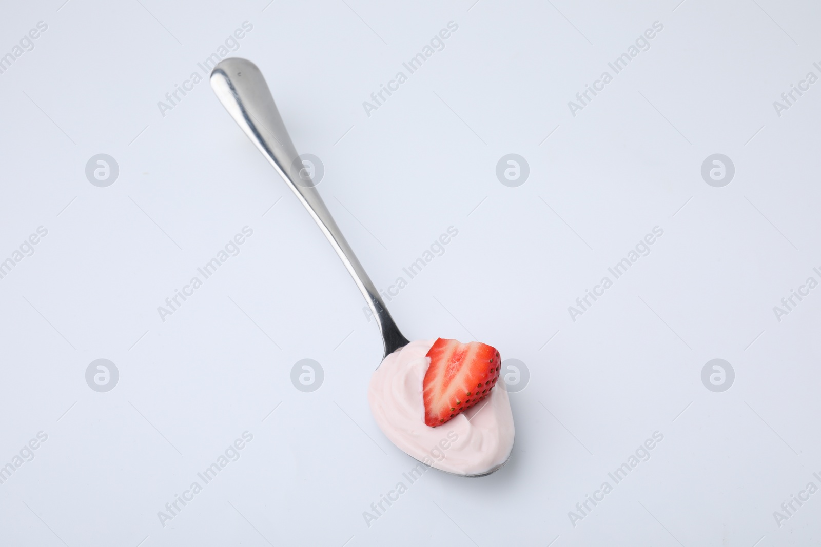 Photo of Delicious natural yogurt with fresh strawberry in spoon on light background