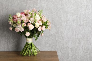 Photo of Beautiful bouquet of fresh flowers on wooden table near grey wall, space for text