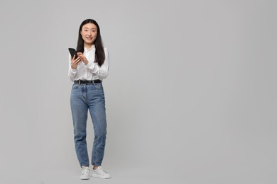 Photo of Full length portrait of smiling woman with smartphone on light background. Space for text