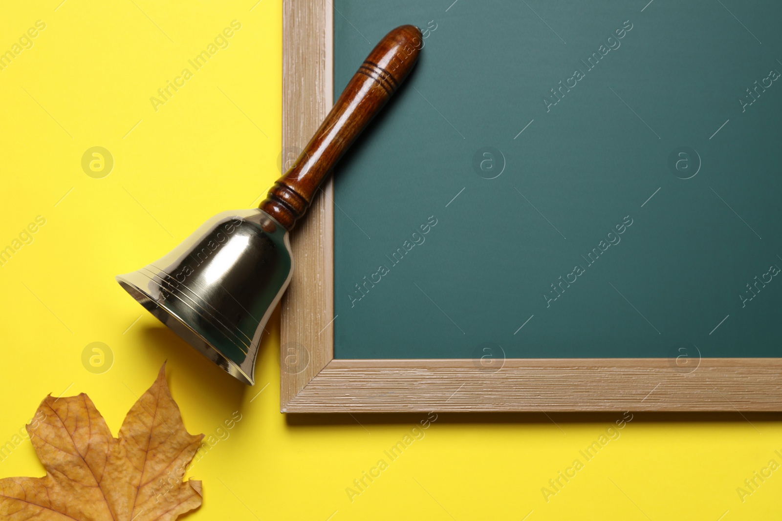 Photo of Golden school bell, green chalkboard and autumn leaf on yellow background, flat lay