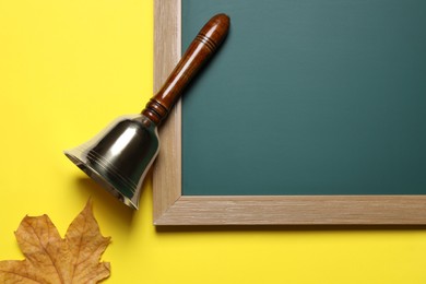 Golden school bell, green chalkboard and autumn leaf on yellow background, flat lay