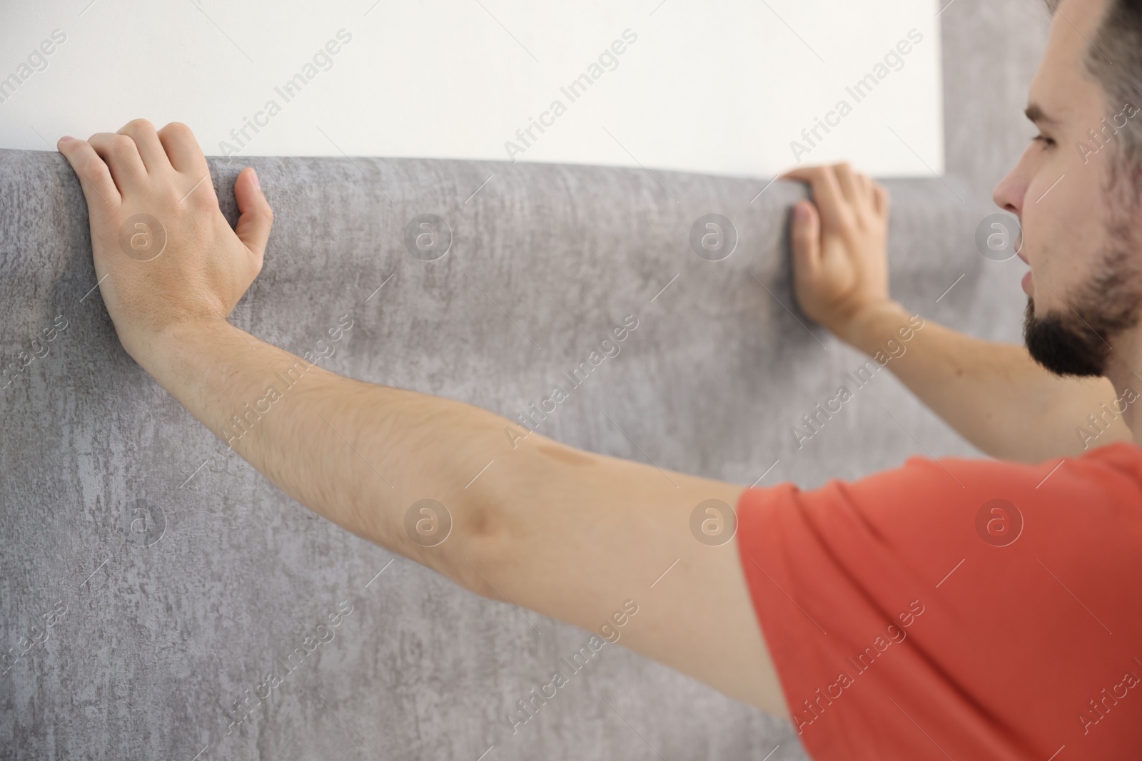 Photo of Man hanging stylish gray wallpaper in room