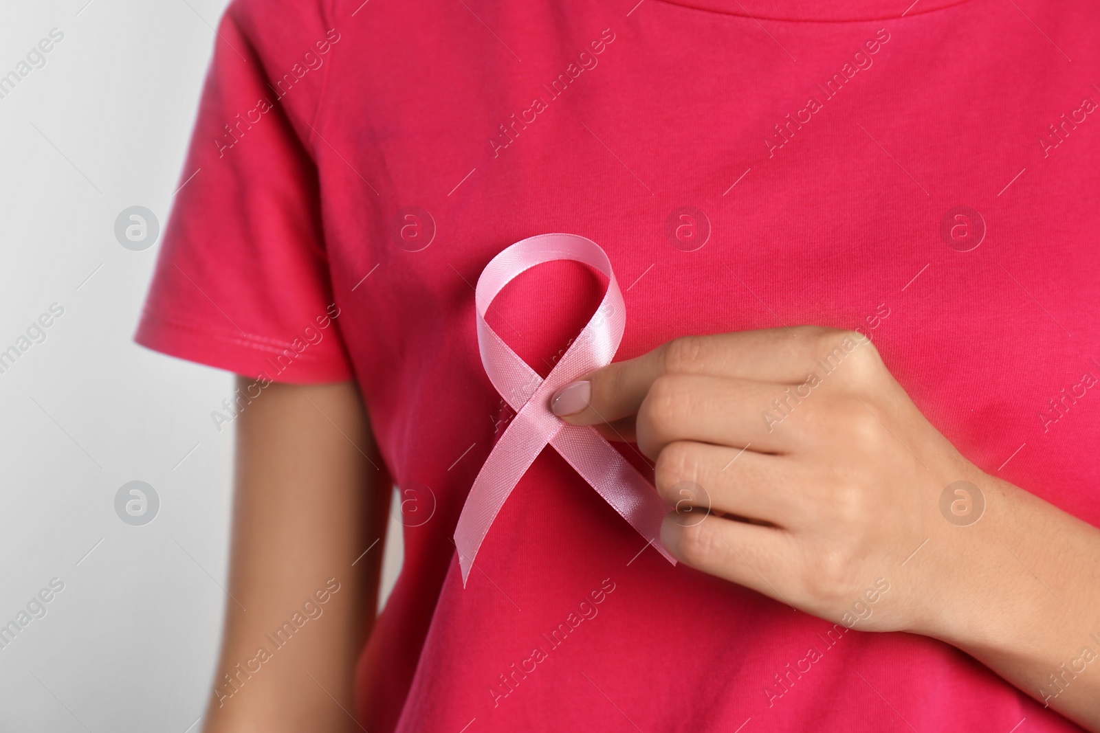 Photo of Woman holding pink ribbon on light background, closeup. Breast cancer awareness