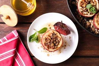 Tasty baked apples with nuts, honey and mint in dishware on wooden table, flat lay