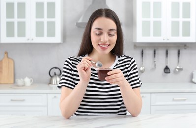 Happy woman with tasty yogurt in kitchen